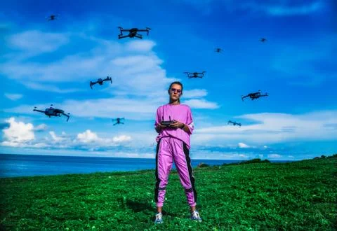 Stylish cool lady surrounded by drones and controls them with remote control Stock Photos