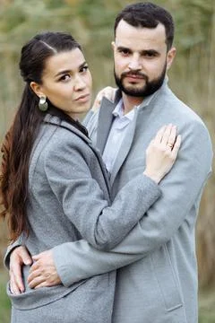 Stylish couple in gray coats gently hugging on the background of reeds. Happy Stock Photos