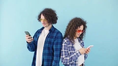 A stylish couple stands backtoback, fully immersed in their smartphones Stock Footage 281037549