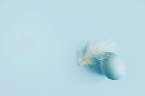 Stylish easter egg and feather on blue background flat lay. Minimal Easter .. Stock Photos