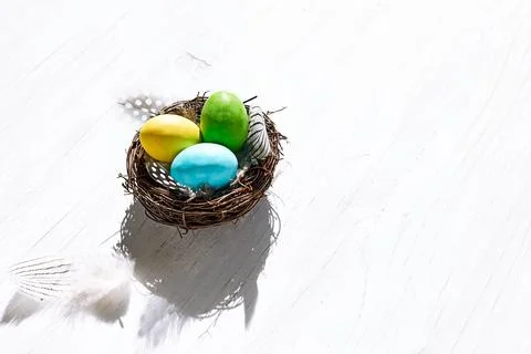 Stylish easter eggs with feathers in the nest on white wooden background. H.. Stock Photos