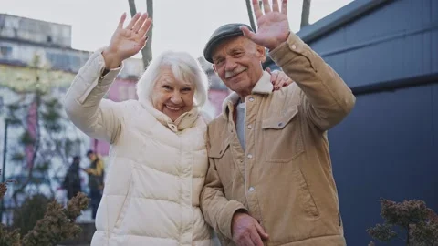 A stylish elderly couple smiling and waving at camera standing on a sunny street Stock-Footage 178950101