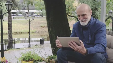 Stylish elderly man smiles looking at tablet screen in cafe 動画素材 146324843
