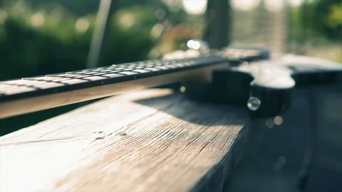 Stylish electric guitar lying on a bench near the metal fence in nature at Stock Footage 99579498