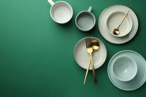 Stylish empty dishware and golden cutlery on green background, flat lay. Spac Stockfoto's