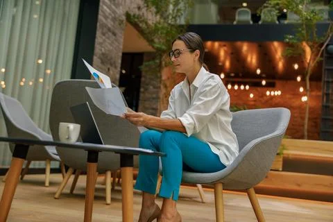 Stylish female analyst working with documents and use laptop in modern office Stock Photos