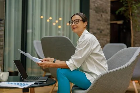 Stylish female analyst working with documents and use laptop while sitting in Stock Photos