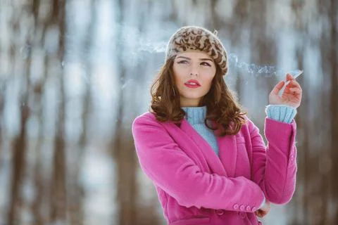 A stylish female in a leopard pattern beret and a pink coat smoking a cigaret 스톡 사진