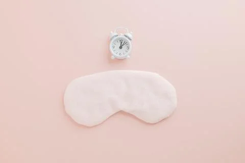Stylish flat lay for World Sleep Day, eye mask and clock on pink background. Stock Photos