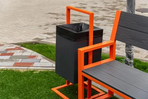 A stylish garbage container is integrated with a bench in a green park area.. Stock Photos