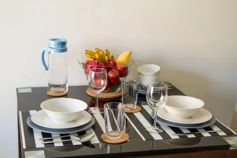 Stylish glass dinning table with table set, glass bowl with fresh exotic fruits Stock Photos