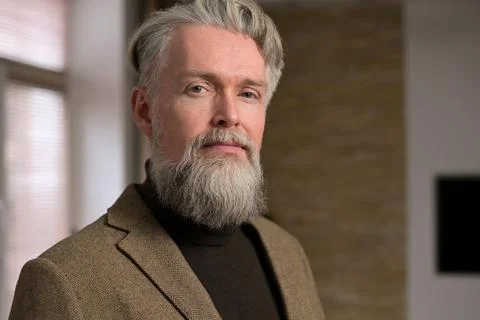 Stylish gray-haired man with a beard in a jacket looks confidently Stock Photos