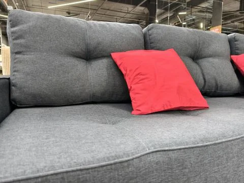 A stylish gray sofa featuring a small red pillow, for sale in a furniture sto Stock Photos