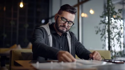 Stylish guy with beard in glasses came in restaurant and choosing food in menu. Stock Footage 100587571