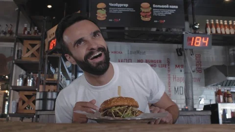 Stylish guy with a beard sits in a cafe at a table with a plate with a burger Stock Footage 115634150