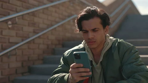 Stylish guy with serious face using smartphone outdoors Stock Footage 163158459