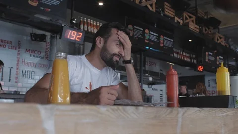 Stylish guy sitting at a table in a cafe swears and gets angry.stained a t-shirt Stock Footage 115634311