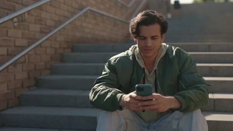 Stylish guy texting on smartphone while sitting outdoors Stock Footage 163829405