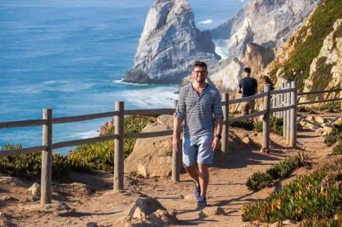 Stylish, handsome guy walking along a gravel road against a background of sea Stock Photos