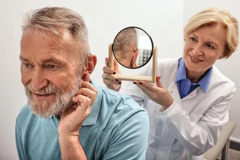 Stylish hearing device. Elderly man with BTE hearing aid looks at himself in  Photos