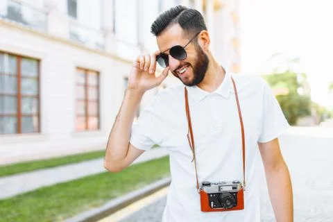 Stylish hipster with a beard and a camera, walking around the city with a cam Stock Photos