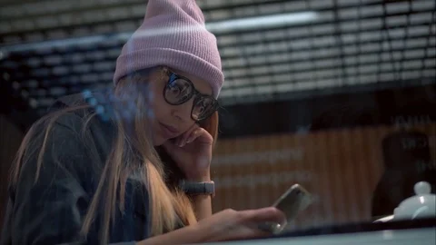 A stylish hipster female in glasses using app on smartphone in a cafe. View Stock Footage 80717883