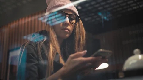 A stylish hipster girl in glasses using app on smartphone in a cafe. View Stock Footage 80718164