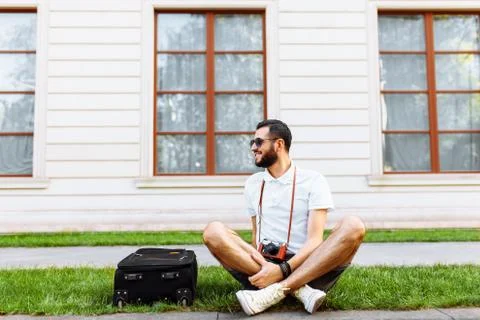 Stylish hipster with a suitcase and a camera sitting on the lawn in the Park 写真素材