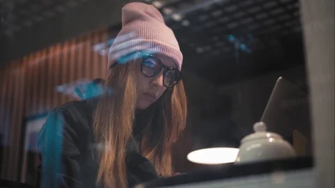 A stylish hipster woman in glasses and hat sitting in cafe and typing with Stock Footage