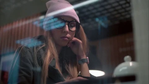 A stylish hipster woman in glasses using app on smartphone in a cafe. View Stock Footage 80718662