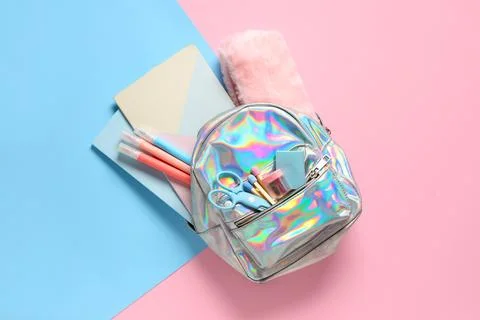 Stylish holographic school backpack with different stationery on color backgr Stock Photos