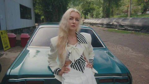 A stylish lady striking a pose beside an oldfashioned car in a city environment Stock Footage 279387360