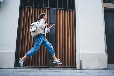 Stylish lady using smartphone while rushing and running along pavement Stock Photos