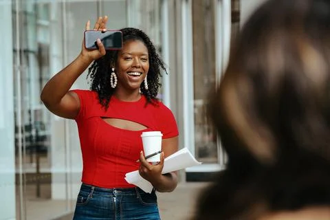 Stylish lady waving with hand while holding coffee, pen and papers in other hand Stock Photos