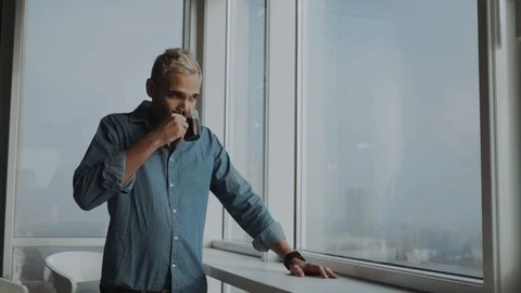 Stylish man with a beard drinking tea / coffee and enjoying the view from the Stock Footage 99913830