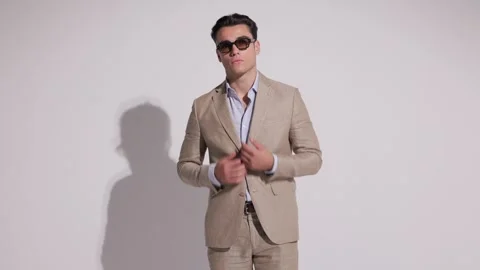 Stylish man in beige suit buttoning jacket, adjusting sunglasses, removing 動画素材 327070085