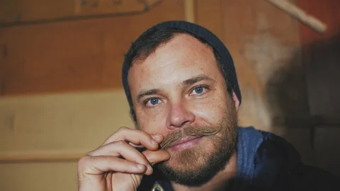 Stylish man with blue eyes with a beard twists his mustache and smiles Stock Footage 103300121