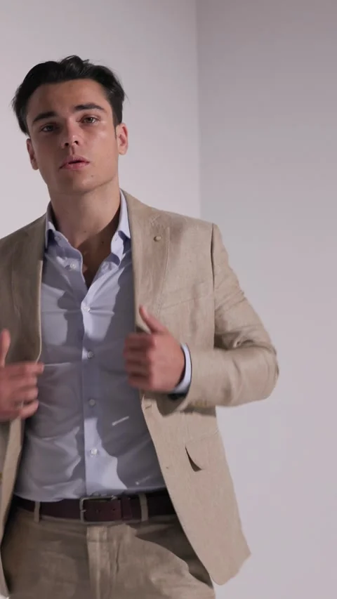 Stylish man buttoning jacket, leaning against wall while looking up, clasping 動画素材 327071578