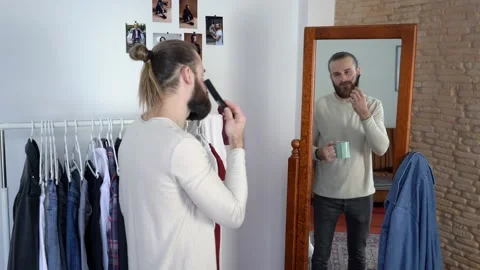 Stylish man is Combing His Beard Drinking  coffee looking at a mirror Stock Footage 147893257