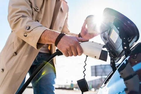 Stylish man inserts plug of the charger into the socket of electric car Stock Photos