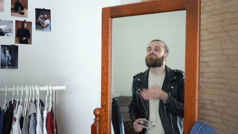 Stylish man in a Leather Jacket is looking into a mirror spraying perfume Stock Footage 147893714