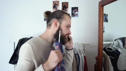 Stylish man is looking in a mirror Choosing what to wear talking on smartphone Stock Footage 147896487
