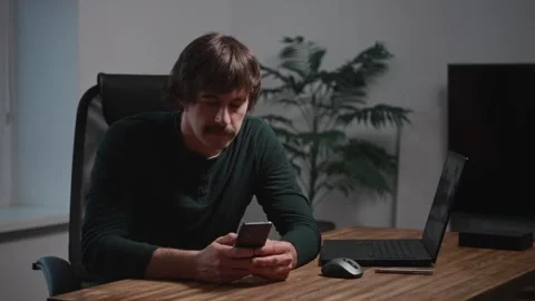A stylish man with a mustache sits at a table using a smartphone. A modern Stock Footage 294162033