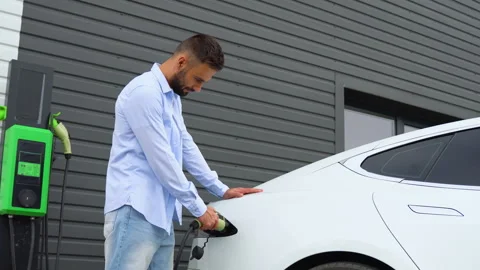 Stylish man plugging in charging cable to electric vehicle and charges batteries Stock Footage 251762508