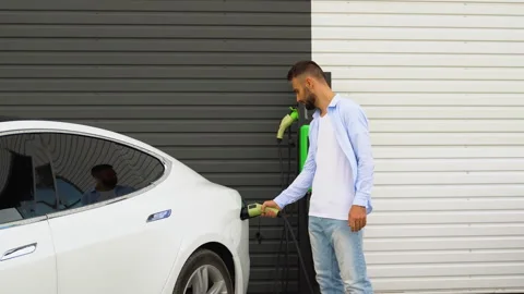 Stylish man plugging in charging cable to electric vehicle and charges batteries Stock Footage 251766602