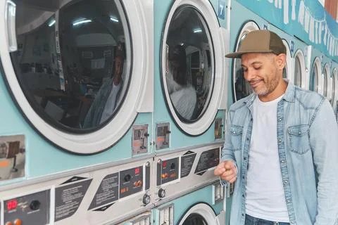 Stylish man smelling laundry detergent pod at laundromat Fotos Stock