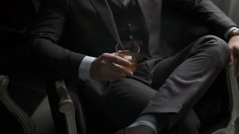 Stylish man in a suit sits on the couch and holds a glass of alcohol. Reflection Stock Footage 142880201