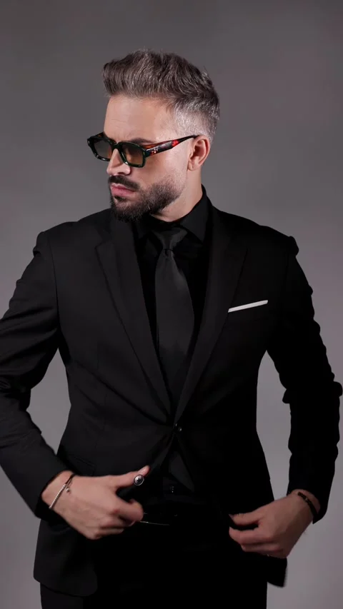 Stylish man in sunglasses is posing with hands in pockets, buttoning his jacket, Video stock 321344418