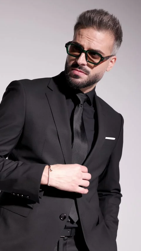 Stylish man in sunglasses is walking, fixing his jacket, arranging his tie, and Vídeo Stock 321345466