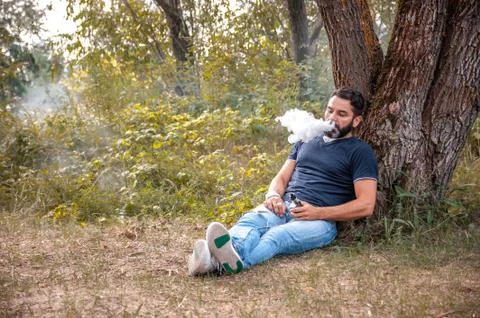 Stylish man vaping an e-cigarette in nature. Vaping concept. Foto stock